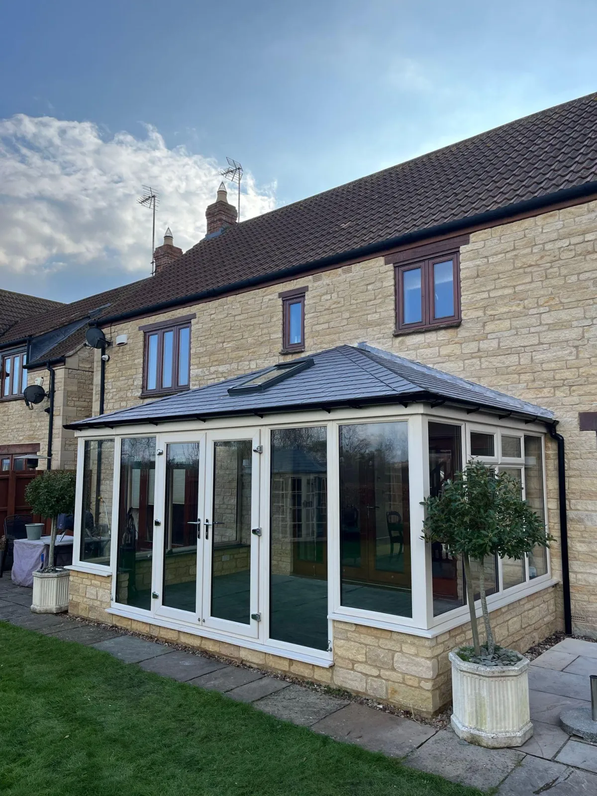 A stylish conservatory extension on a stone-built home, featuring a tiled roof with a Velux window for added natural light.