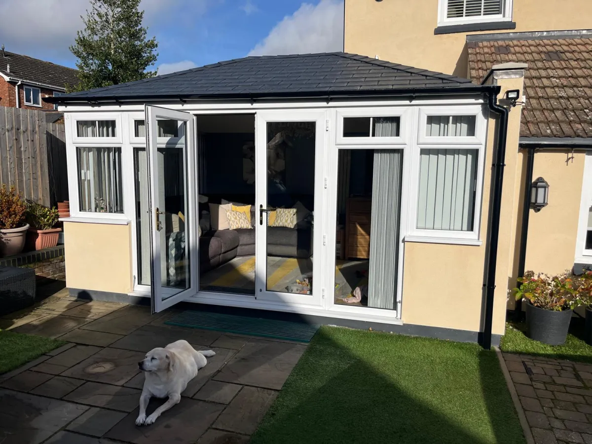 A warm and inviting conservatory with French doors opening onto a beautifully maintained patio, complete with a happy Labrador enjoying the sunshine.