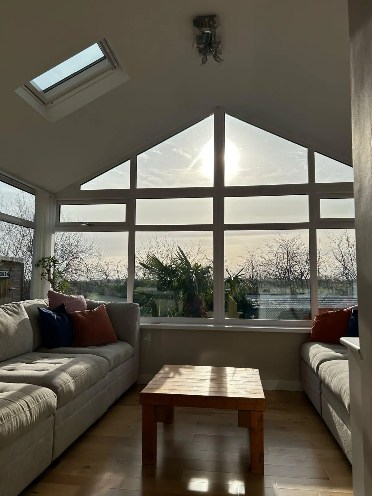 A stylish conservatory interior featuring a vaulted ceiling with Velux windows, allowing natural light to flood the space. The cozy seating area creates the perfect indoor-outdoor retreat.