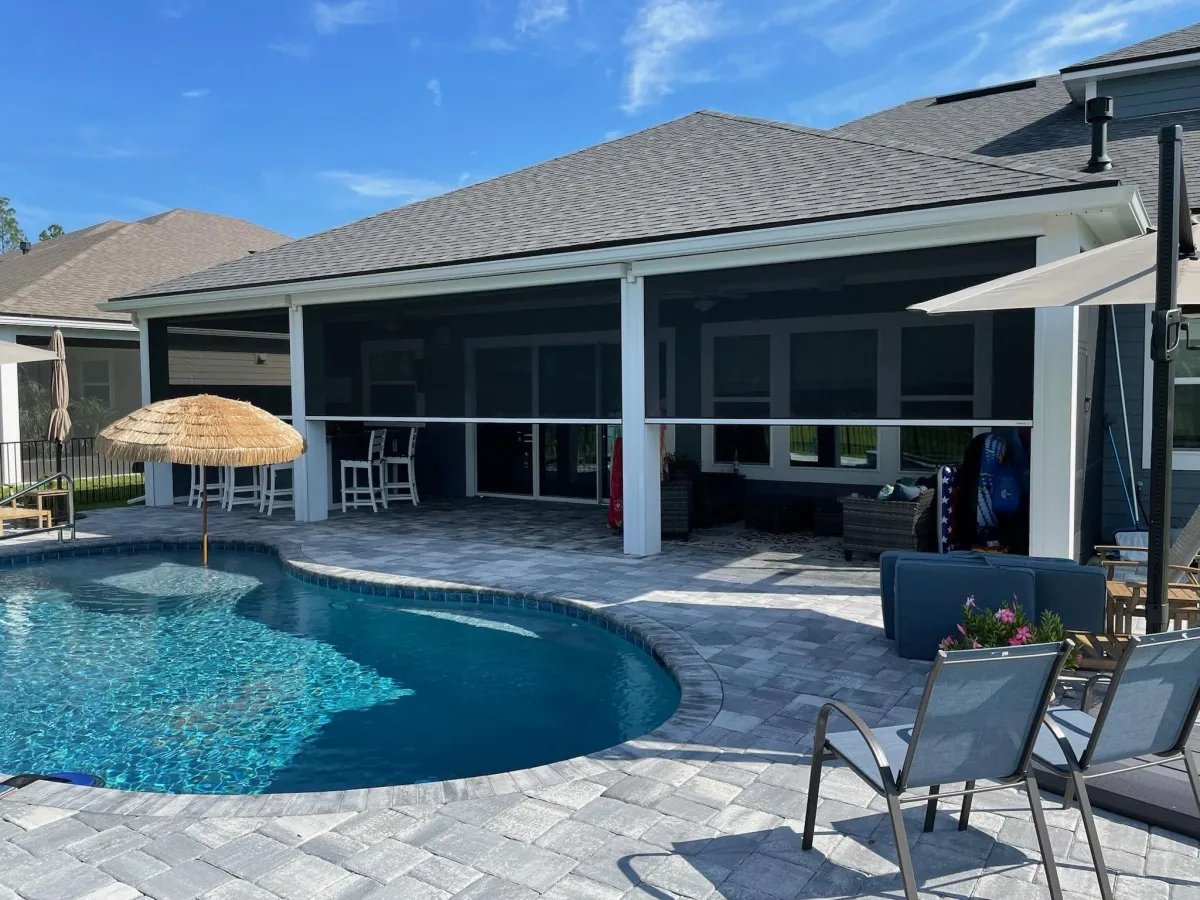 A large white house featuring elegant black MagnaTrack Motorizeed Screens, set against a clear blue sky.