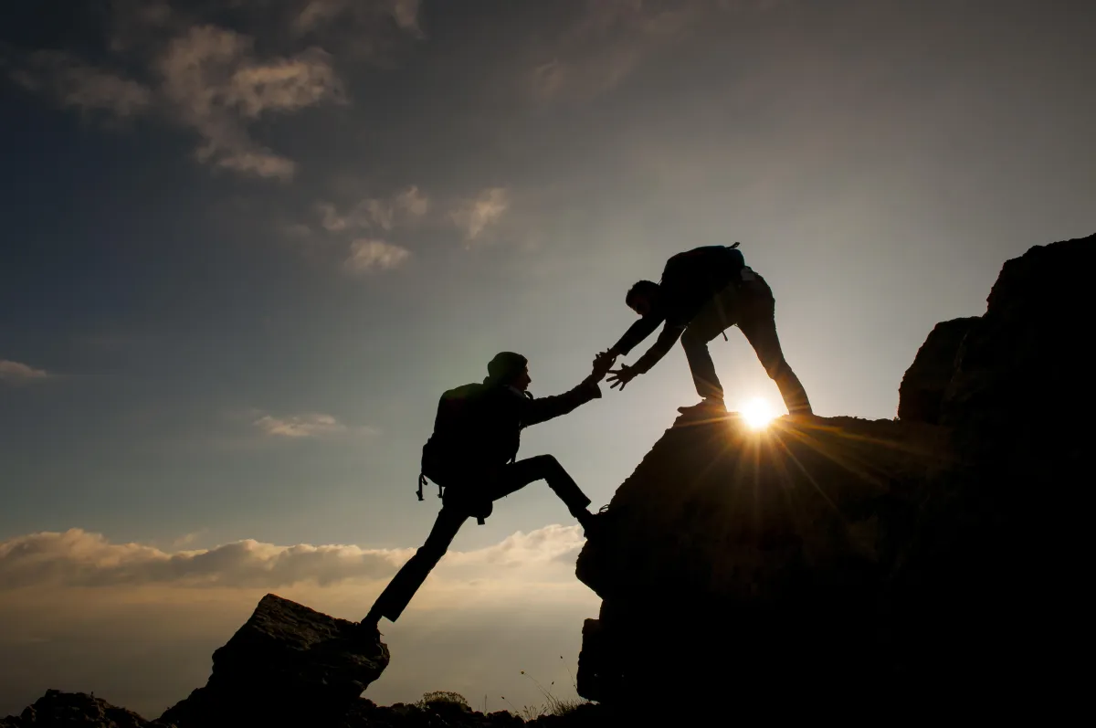 Person helping somebody else to climb a mountain