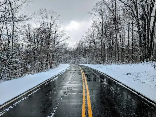 Snow-covered rural road with icy conditions and bare trees, illustrating winter driving challenges in New Jersey.