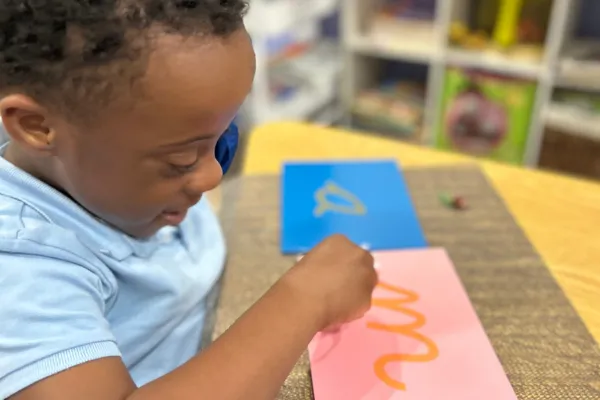 Child tracing cursive Sandpaper Letters and smiling