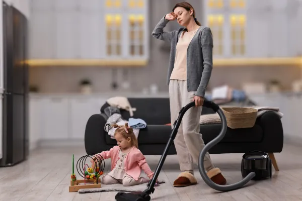 Tired exhausted mom vaccumming while child plays on floor
