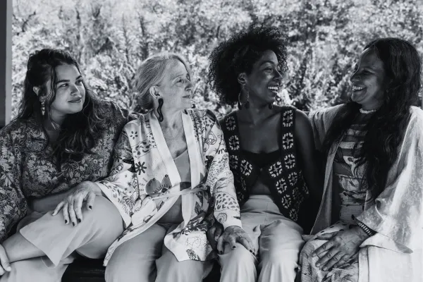 Four middle-aged women sit on a bench chatting and smiling with each other