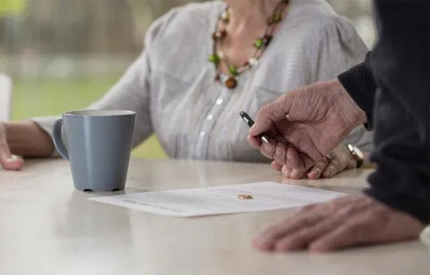 Close-up of hands signing legal documents with a cup and wedding ring on the table, symbolizing the role of marriage length in alimony decisions as evaluated by West Virginia courts.
