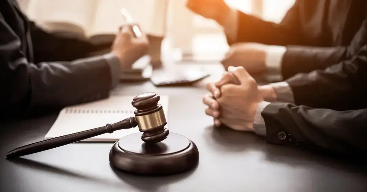 Judge’s gavel on a table with people in business attire discussing legal documents in the background.