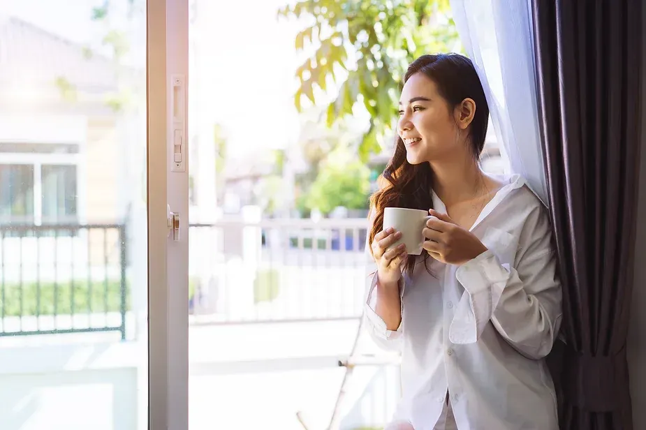 Woman standing in window with morning coffee