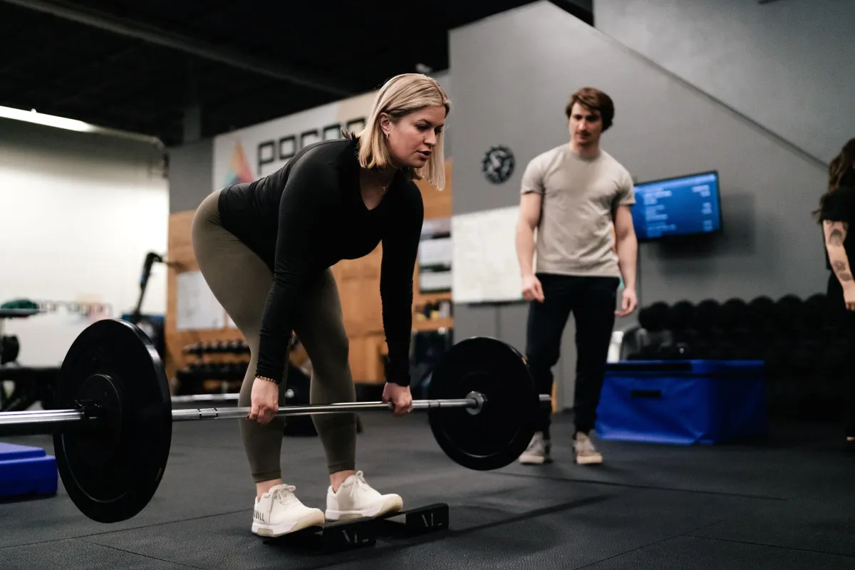 Image of a client lifting a barbell with a coach watching their form.