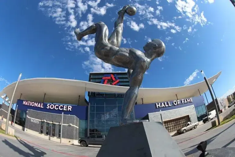 Metal statue of a soccer player mid-bicycle kick in front of the National Soccer Hall of Fame.