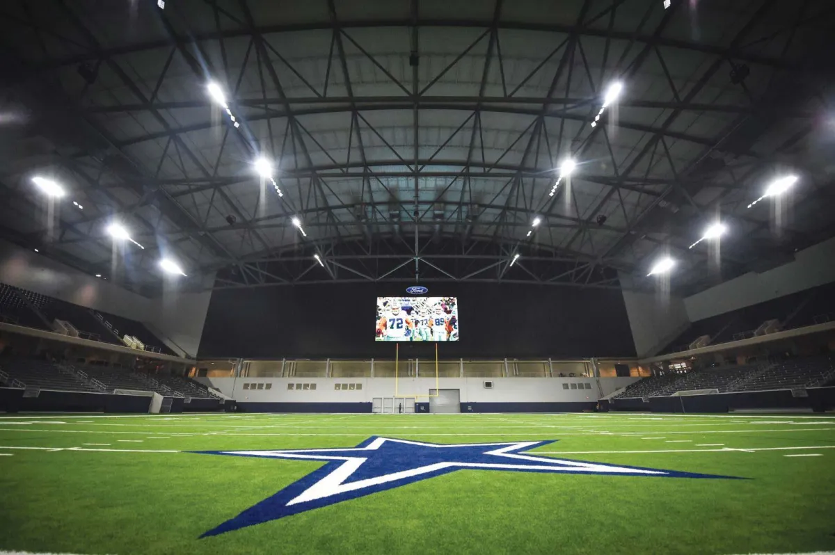 Dallas Cowboys' indoor stadium with turf, scoreboard, and steel beam ceiling.