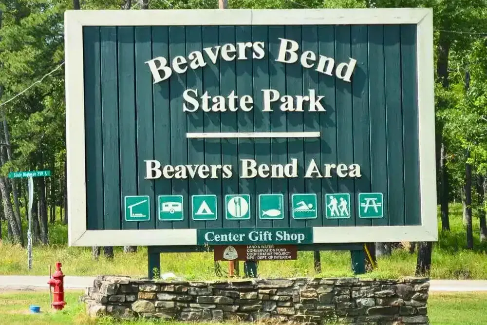 Wooden park sign with activity icons, stone base, and scenic backdrop.