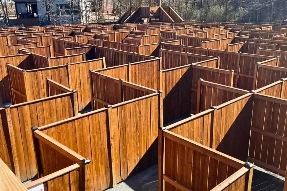 Large wooden maze with pathways and central observation tower outdoors.