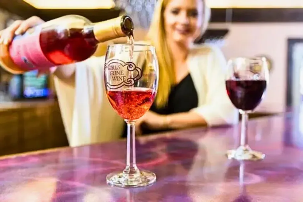 Person pouring rosé wine into a glass, showcasing bar ambiance.