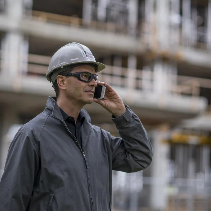 Phil wearing a hard hat and safety glasses,  talking on his cell phone on a construction site