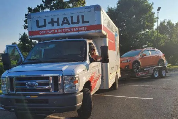 Claudette driving a U-Haul with her orange Subaru in tow, marking a five-year anniversary of her move south to rebuild life and legacy