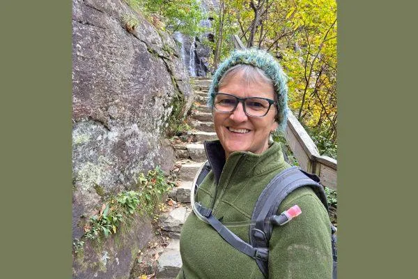 Claudette smiling on a peaceful mountain trail beside a waterfall, symbolizing calm strength and growth.