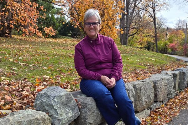 “Claudette Eames sitting on a stone wall in autumn, symbolizing calm strength and balance.”