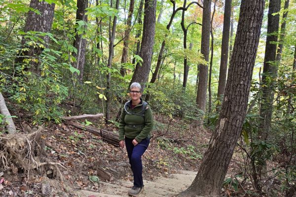 Woman walking a wooded trail, reflecting on building a business that fits the life she’s grown into through calm, strength, and personal growth.