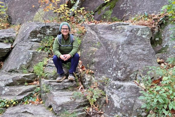 Claudette seated on stone steps in a wooded setting, reflecting on grief, nervous system healing, and carrying love in a new way.