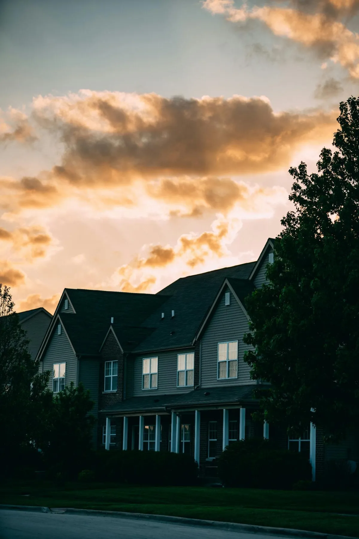 Row of suburban houses under a sunset sky with scattered clouds.