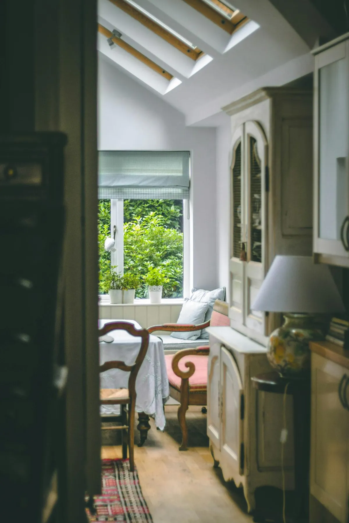 A cozy sunlit reading nook with a window seat, vintage wooden furniture, and potted plants adding a natural touch to the serene space.