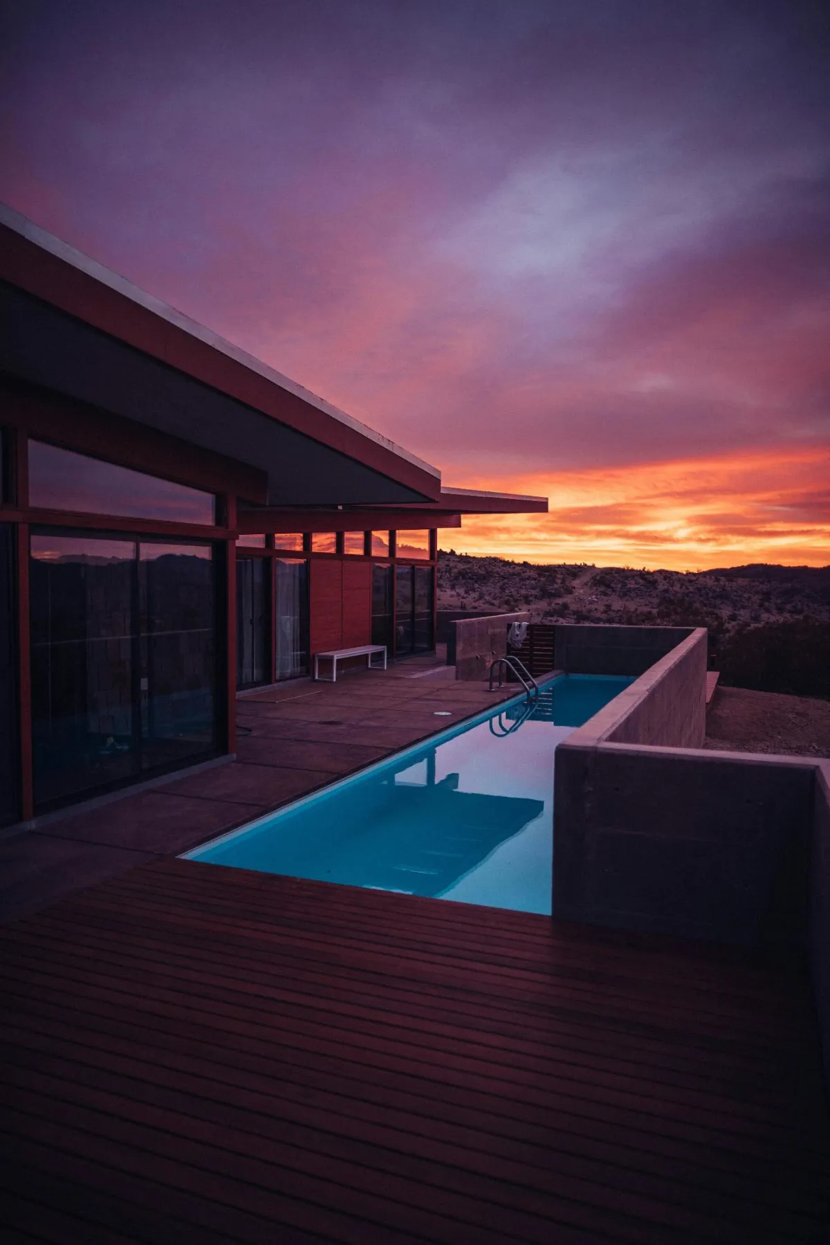 A modern home with a sleek infinity pool reflecting a vibrant sunset over a desert landscape.