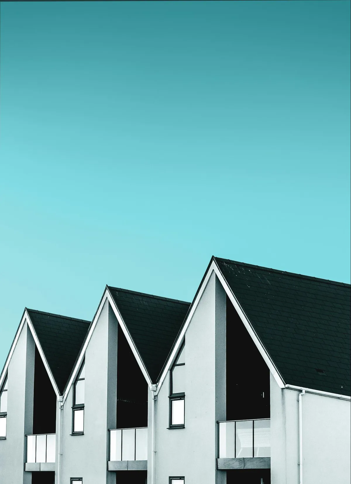 A row of modern houses with sharp triangular roofs against a turquoise sky.