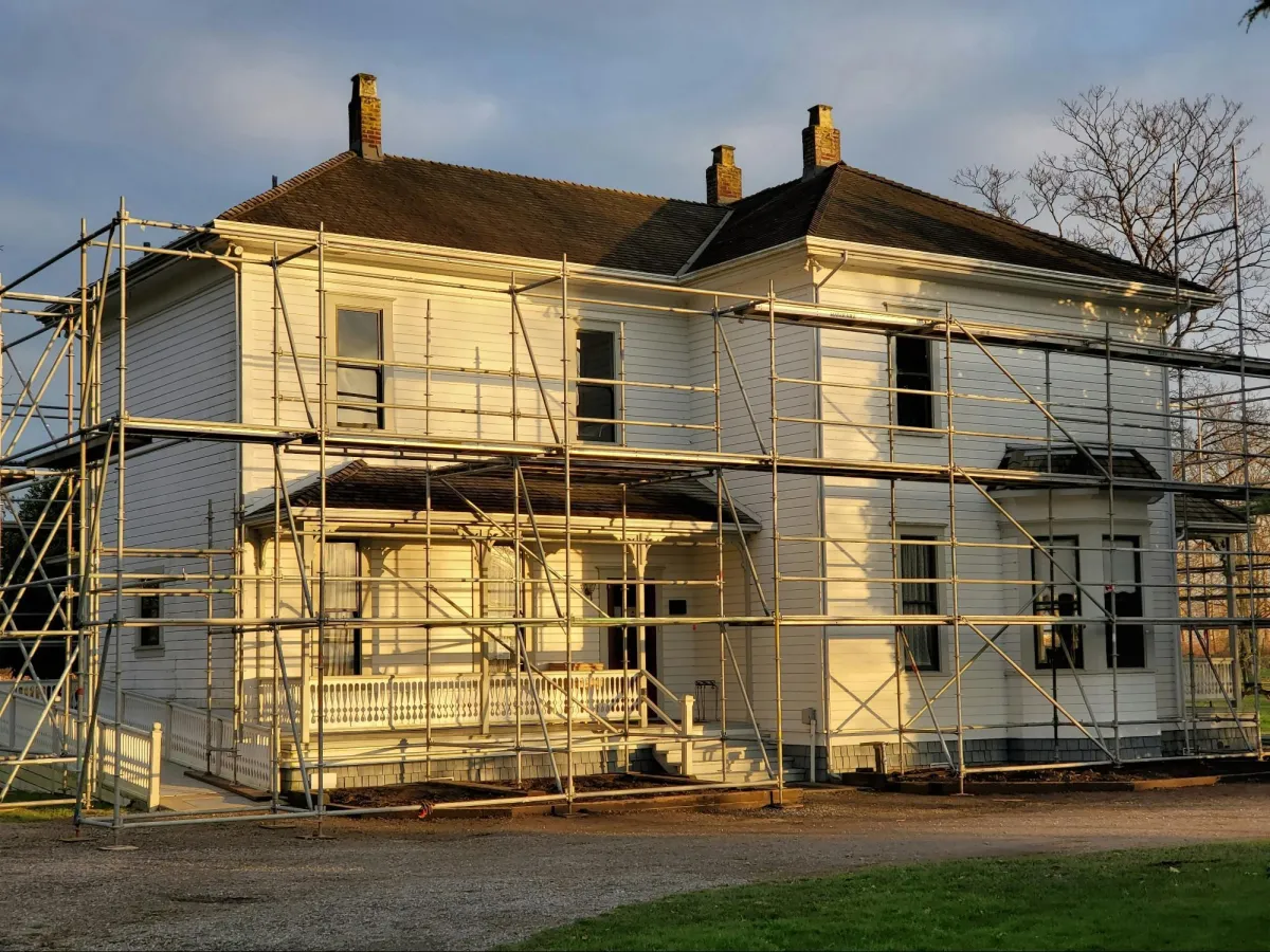 A large white house surrounded by metal scaffolding, undergoing renovation or construction work