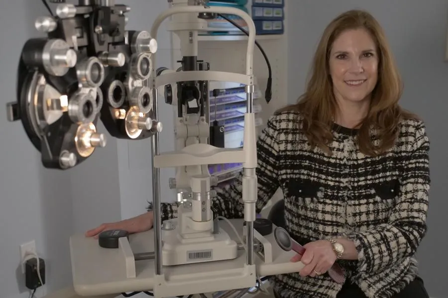 Optometrist in an eye exam room with specialized equipment, smiling and ready to conduct a thorough eye examination for patients.