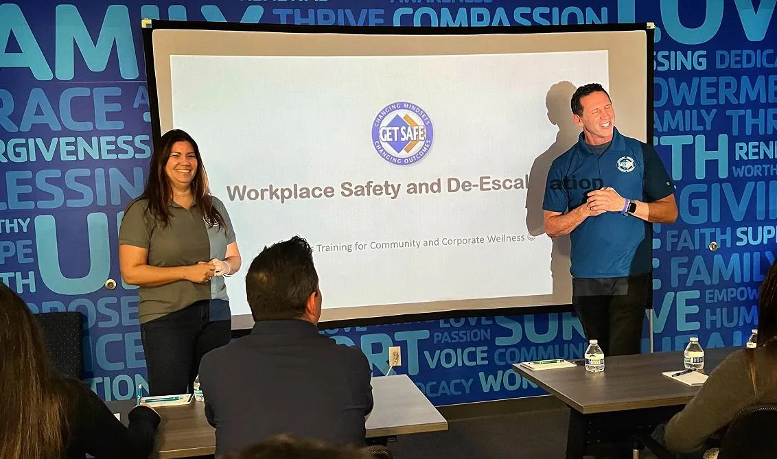 Two speakers (a man and a woman) present “Workplace Safety and De-Escalation” training to an audience.
