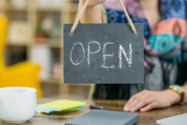 upclose image of a person holding up a chalkboard sign with the word OPEN. The word open is written in chalk.