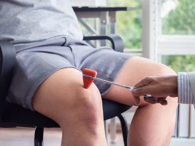 Doctor testing a patient’s knee reflex with a red reflex hammer.