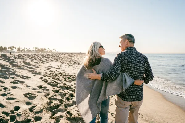 Smiling retired couple walking on the beach at sunrise, representing financial independence and early retirement planning success.