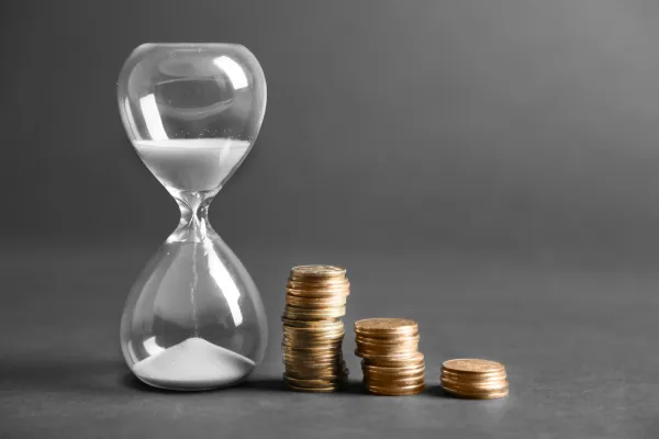 Hourglass next to stacked coins symbolizing the importance of starting early with investing and how time impacts financial growth.