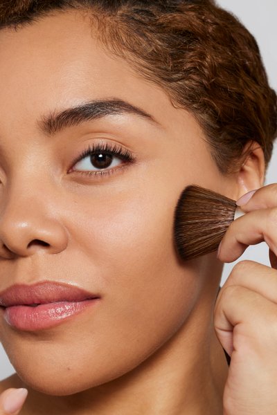 Woman applying Jane Iredale mineral foundation with a makeup brush, showing natural, healthy-looking skin