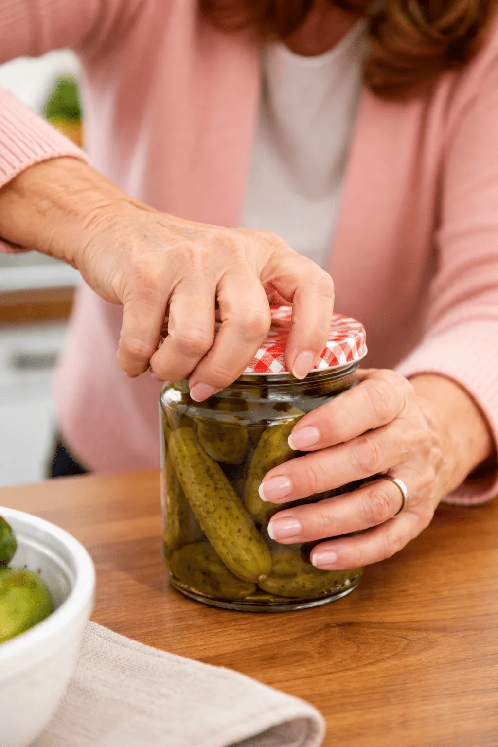 Mano di una donna adulta che cerca con difficoltà di aprire il tappo di un barattolo in cucina, evidenziando dolore e rigidità alla base del pollice tipici della rizartrosi.