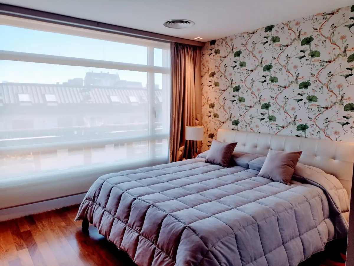 Habitación con la pared estilizada con papel tapíz, ventanas con cortinas blackout y láminas de control Solar