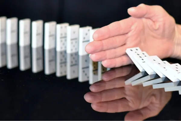 the image shows a line of tumbling dominos across the screen.  Half way there is a hand interrupting the line stopping the remaining dominos from falling.