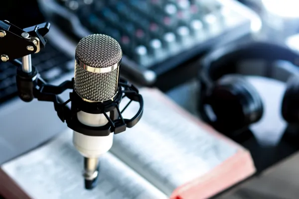 Image shows a clos up of a desk with a professional microphone suspended above it, with an open book and a headphones on the desk.