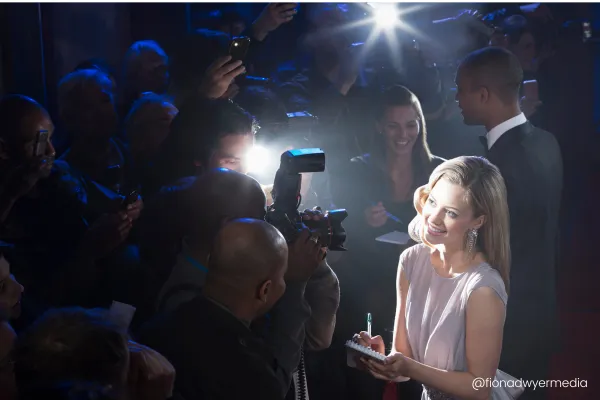 Image shows celebrities on the red carpet having their photos taken in a media huddle. 