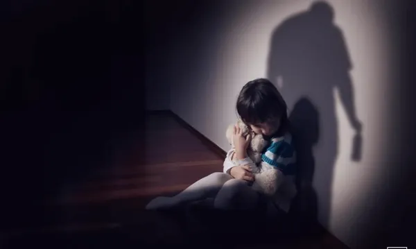 girl hugging teddy bear sitting on floor in dark room