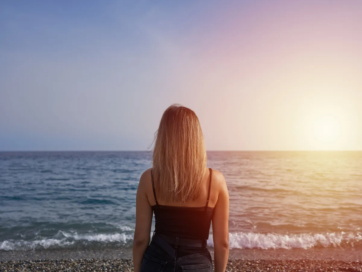 A woman standing on a serene beach at sunrise, looking toward the horizon, symbolizing clarity, transformation, and new beginnings.