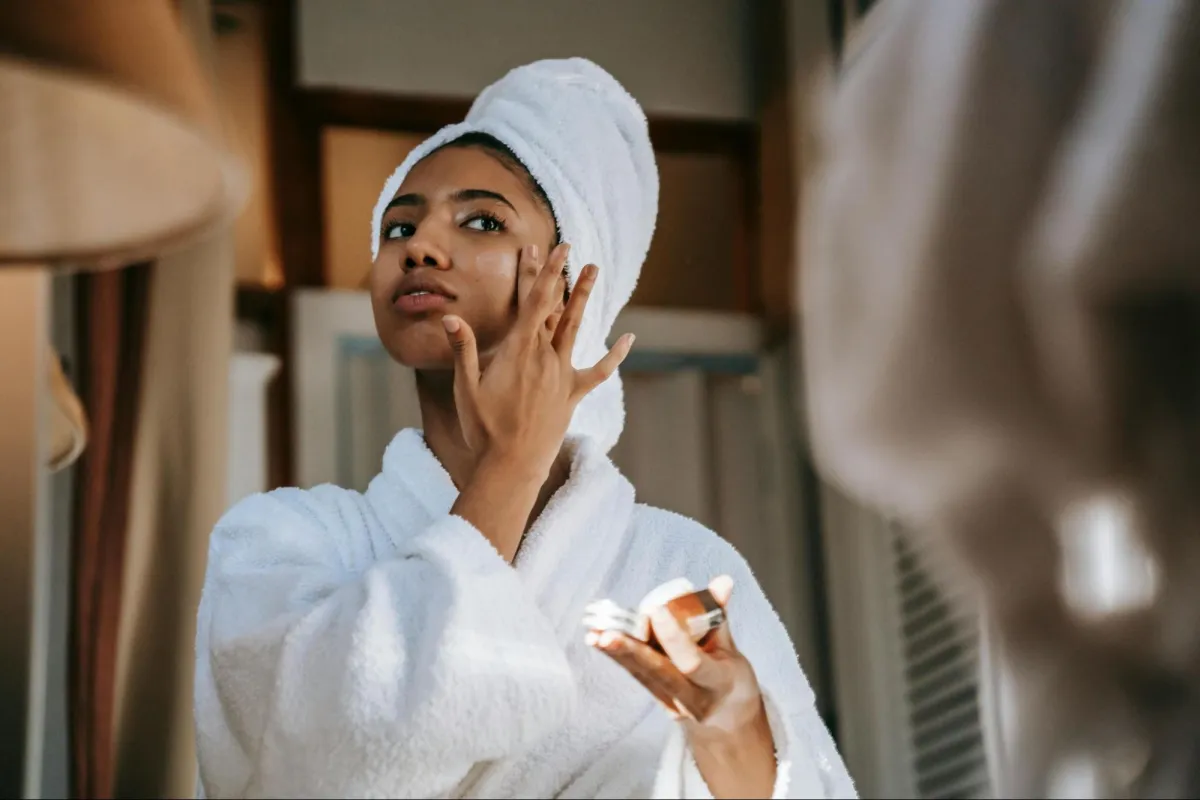 woman applying cream on the face against the mirror