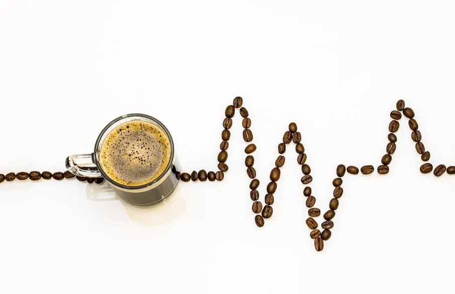 Coffee beans in the shape of a heart monitor with a cup of coffee in the middle.