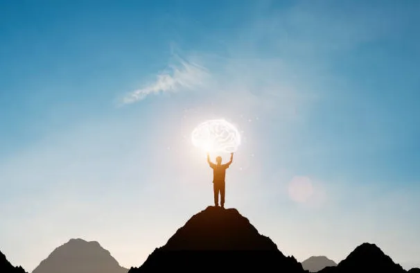 Man holding up glowing brain on a mountain top exhibiting mental fitness.