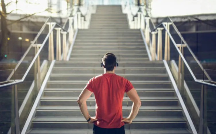 Athletic man with hands on hips in workout gear at the bottom of a staircase facing upwards as he prepares to begin a workout.