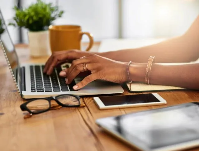 Woman typing on laptop with glasses and a mug next to her