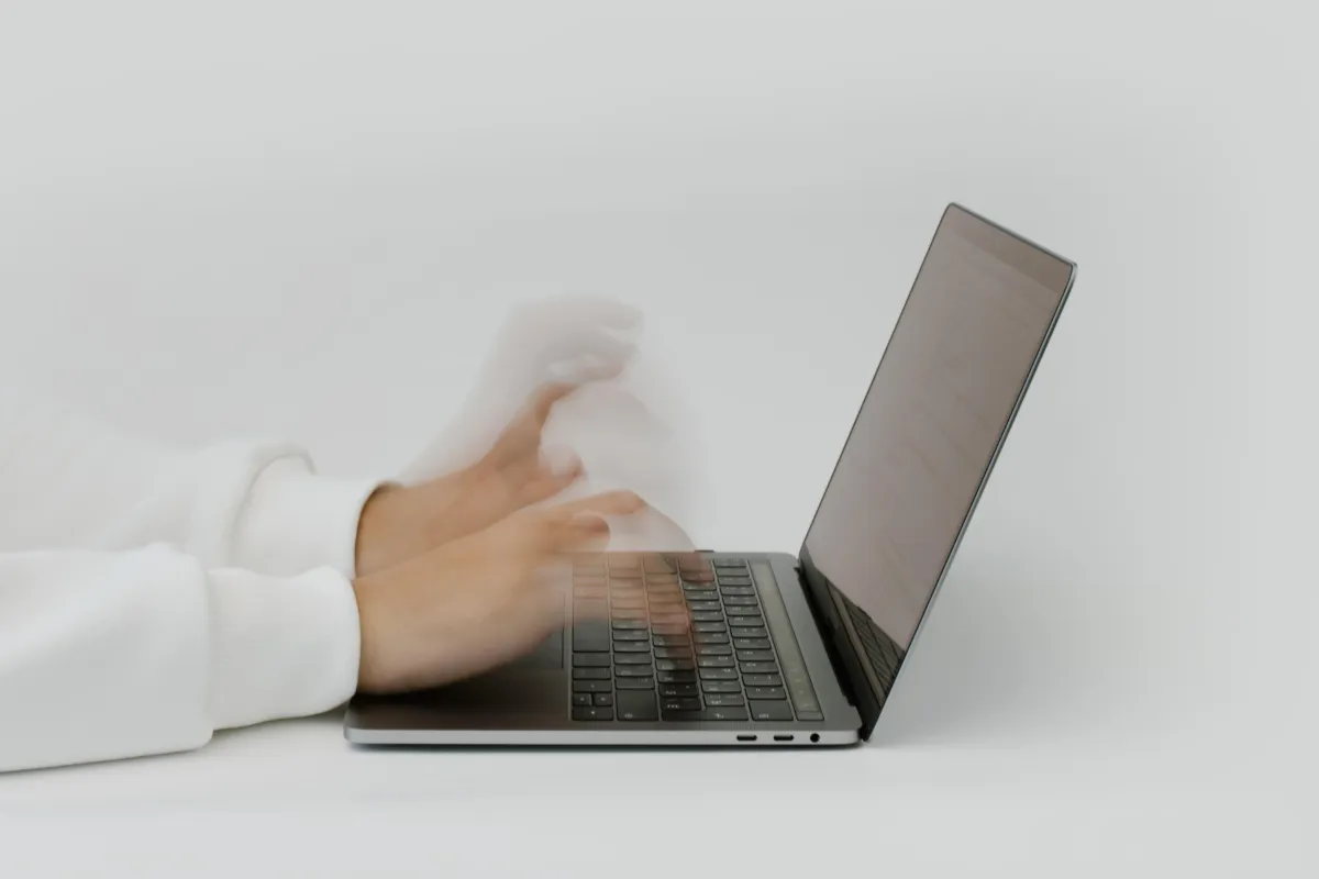 Hands typing so fast on a laptop that they are blurry