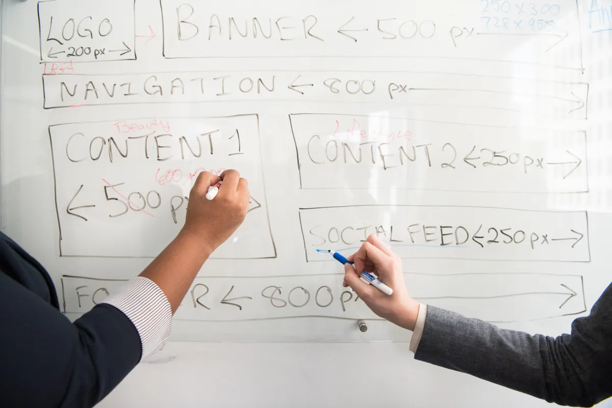 Two hands holding markers writing on a whiteboard about marketing strategies